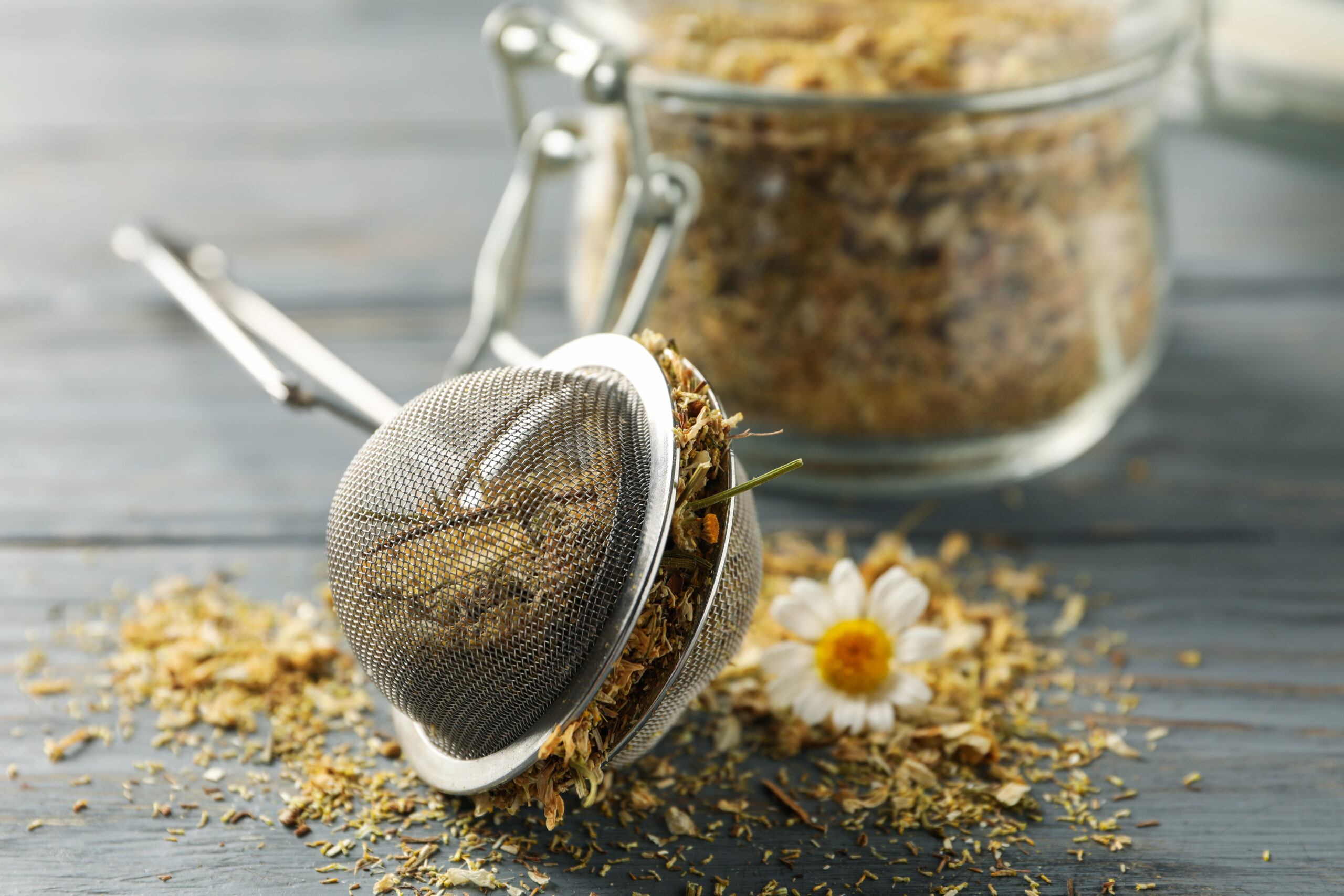Glass jar and sieve with dried chamomile on gray wooden background