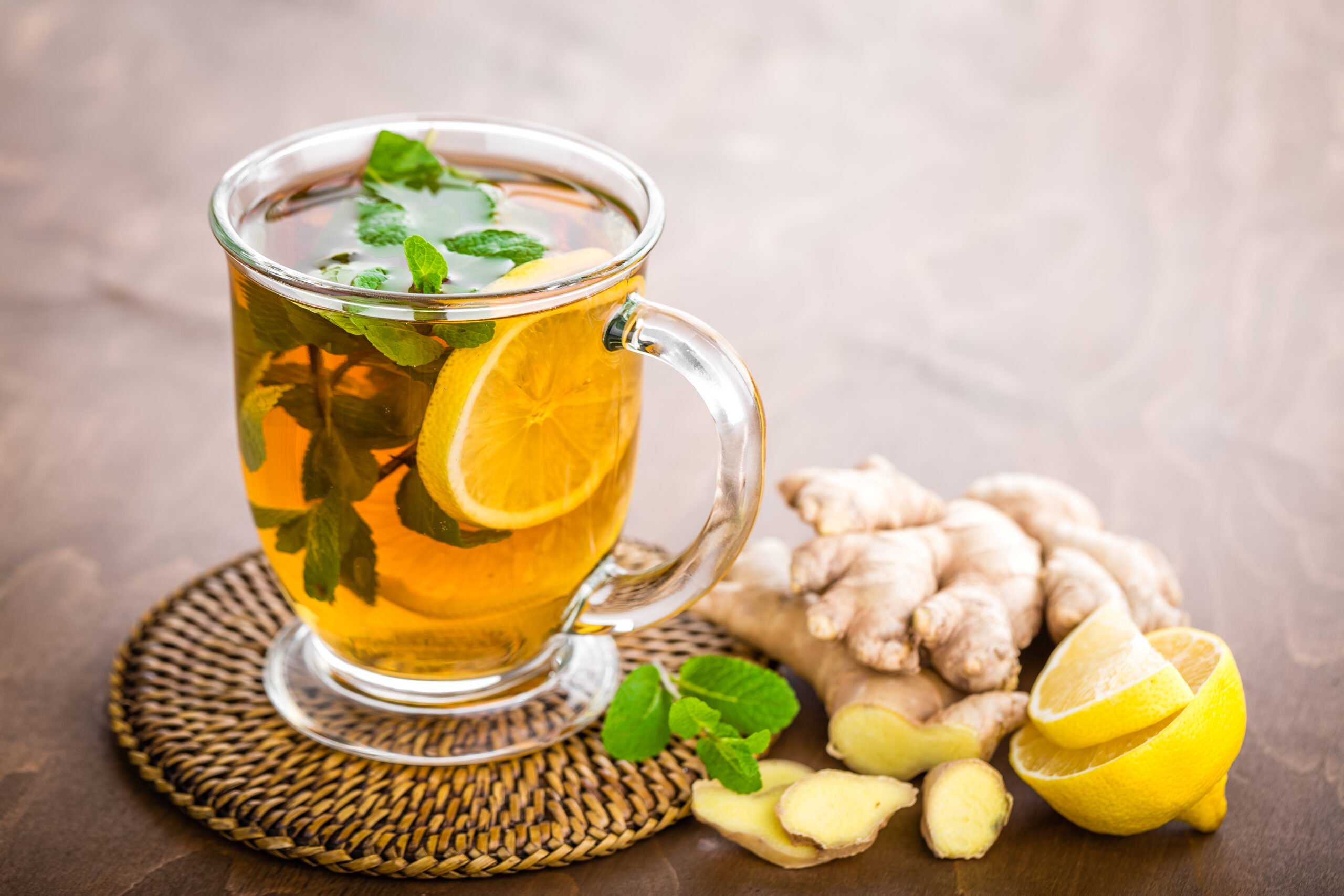Hot herbal tea with fresh lemon, ginger and mint leaves on brown background, closeup